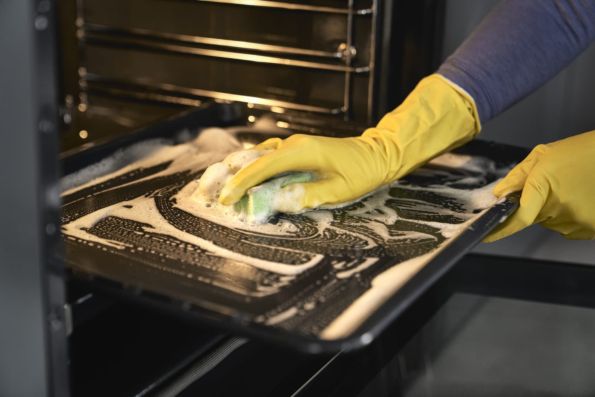 An operator in gloves deep-cleaning an oven tray with eco-friendly foam