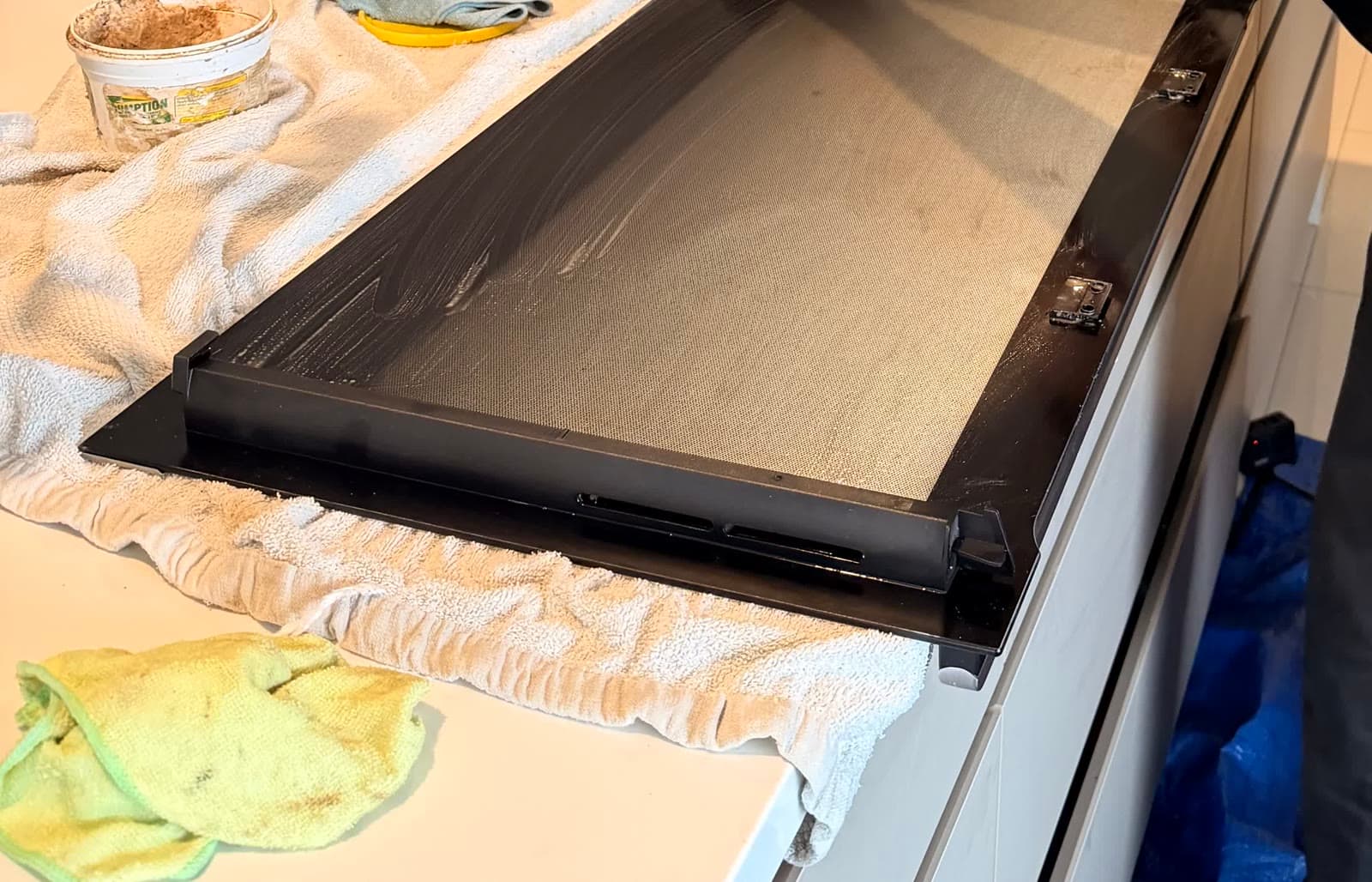 An oven door removed from the appliance and dismantled on a protected benchtop, with the inner glass panel separated from the frame during an Oven Valets clean.